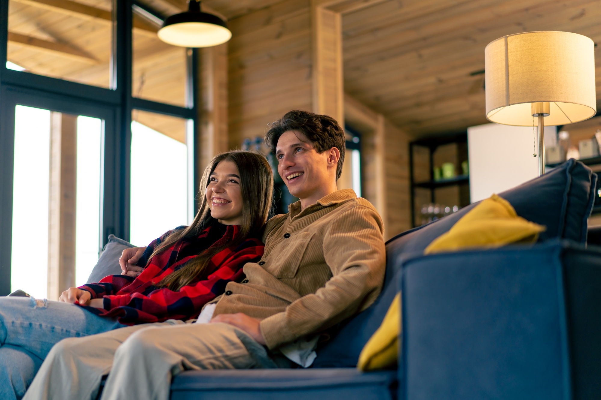 A young couple in love together sitting on the sofa at home watching a comedy film and laughing